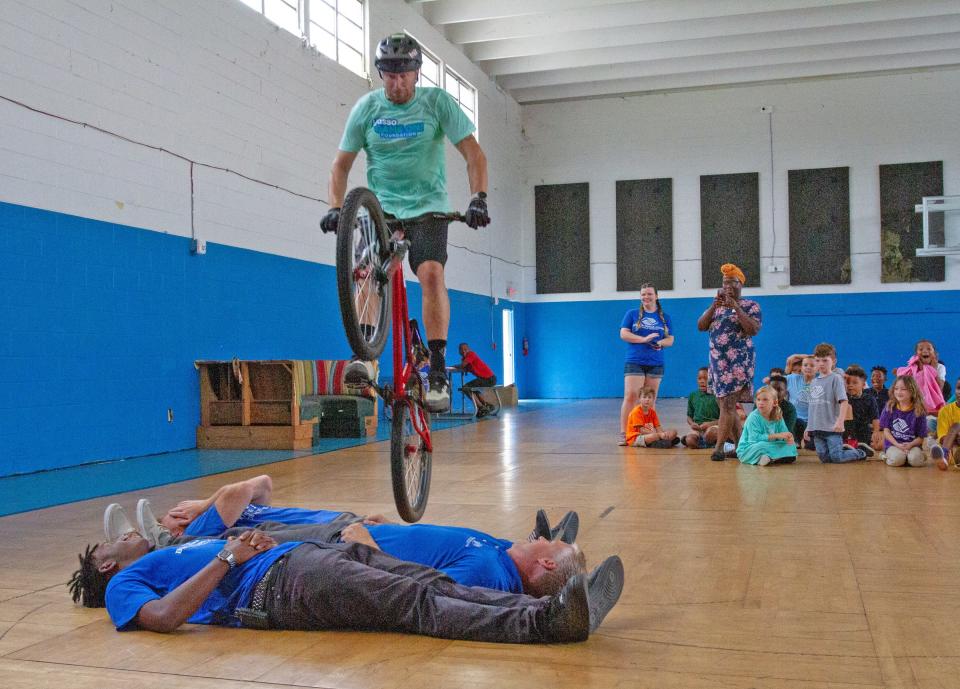 Jeff Lenosky, a professional mountain bicyclist, hops over three staff members from the Boys and Girls Clubs of Polk County at the James J. Musso Unit on Wednesday afternoon. Lenosky put on a display of tricks before children in the program received free bicycles.