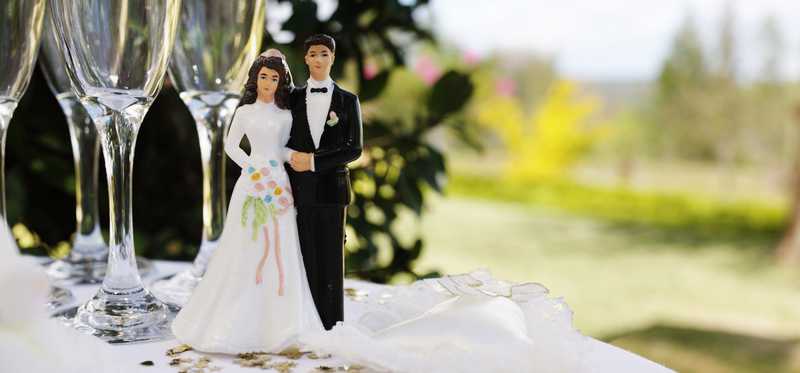 Wedding couple figurines on a glitter-covered white tablecloth and champagne glasses.