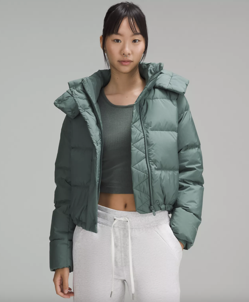 asian model wearing light grey sweatpants, green cropped tank top and green puffer coat, Wunder Puff Cropped Jacket in Medium Forest (Photo via Lululemon)