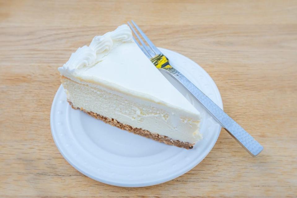 Slcie of cheesecake with graham-cracker crust on white plate with a fork next to it 
