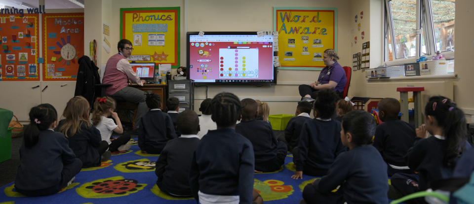 Alex Dickerson the reception class teacher, left leads the class at the Holy Family Catholic Primary School in Greenwich, London, Monday, May 24, 2021. Holy Family, like schools across Britain, is racing to offset the disruption caused by COVID-19, which has hit kids from low-income and ethnic minority families hardest. (AP Photo/Alastair Grant)