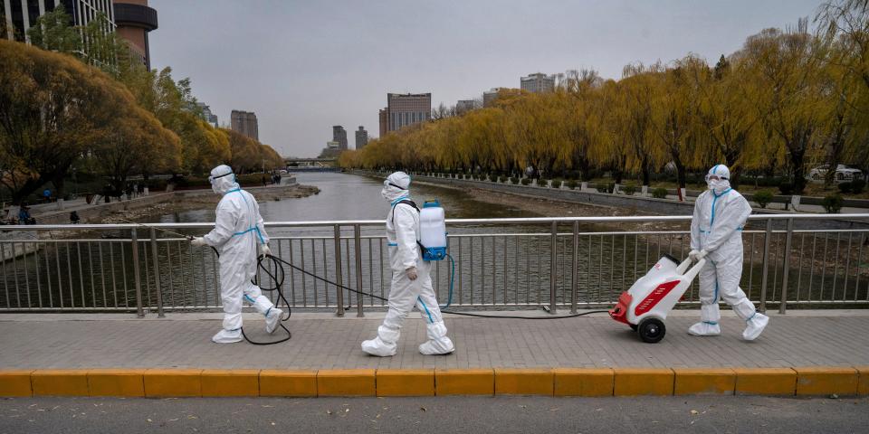 Workers in full-body hazmat suits walk on a bridge.