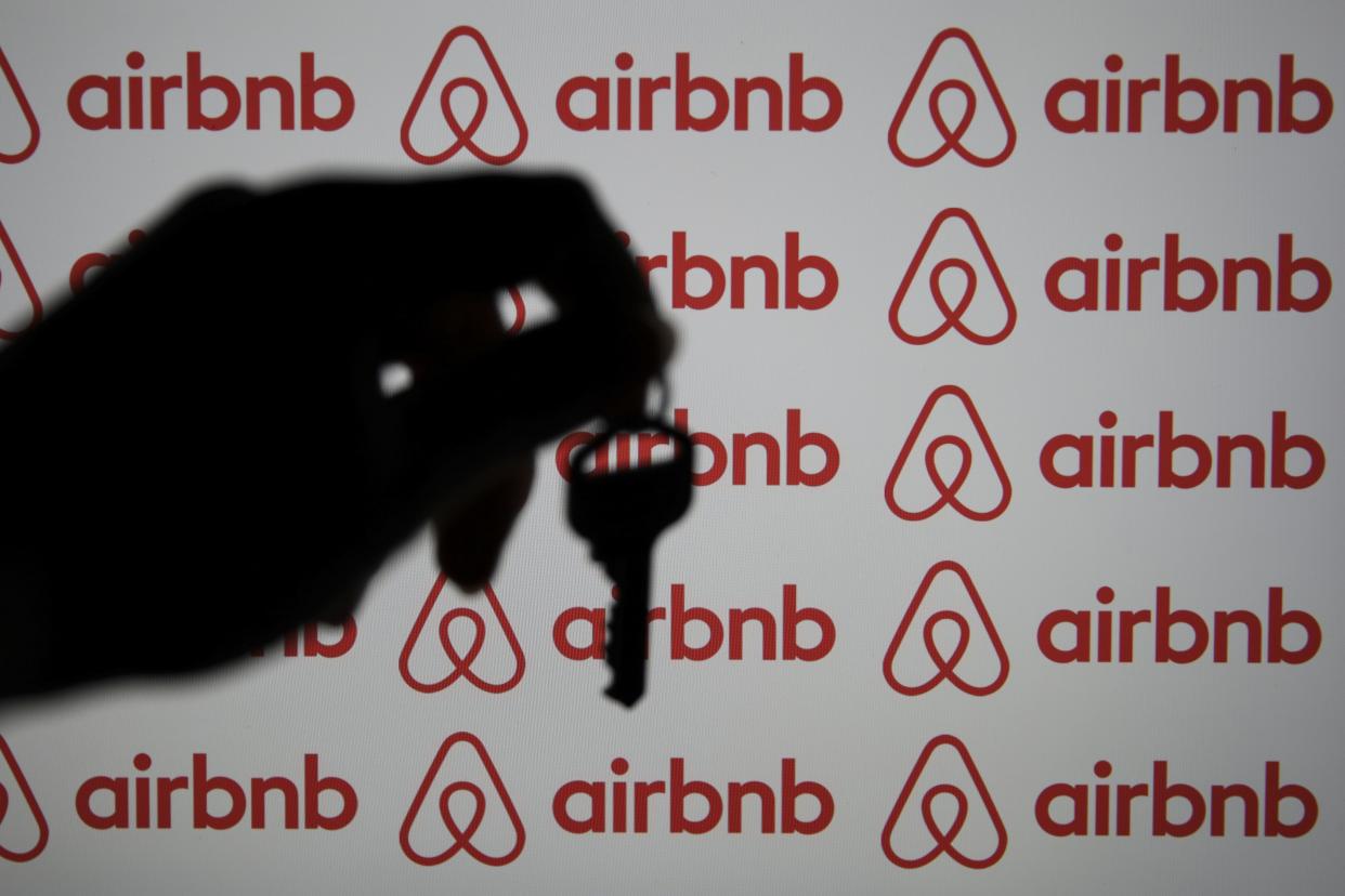 The shadow of a hand holding a key in front of a group of Airbnb logos.