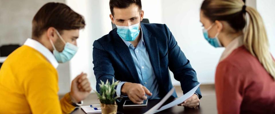 Financial advisor going through paperwork with a couple in the office and wearing face mask due to COVID-19 pandemic.