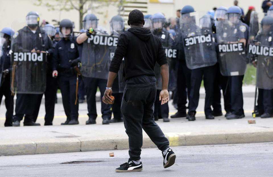 A demonstrator walks past police with a brick as they respond to thrown objects, Monday, April 27, 2015, after the funeral of Freddie Gray in Baltimore. Gray died from spinal injuries about a week after he was arrested and transported in a Baltimore Police Department van. (AP Photo/Patrick Semansky)