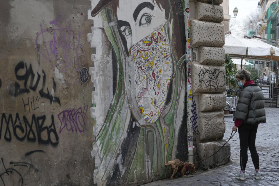 A woman wearing a surgical mask walks a dog in Rome, Sunday, Jan. 9, 2022. Italy, Spain and other European countries are re-instating or stiffening mask mandates as their hospitals struggle with mounting numbers of COVID-19 patients. (AP Photo/Gregorio Borgia)