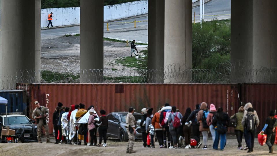 A Mexican security guard is seen across the border in Piedras Negras, a city in Mexico, as immigrants wait to be processed at a US Border Patrol transit center after crossing the border at Eagle Pass, Texas, on December 22, 2023. - Chandan Khanna/AFP/Getty Images