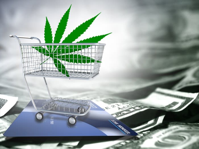 Cannabis leaf inside a miniature shopping cart on top of a pile of cash.