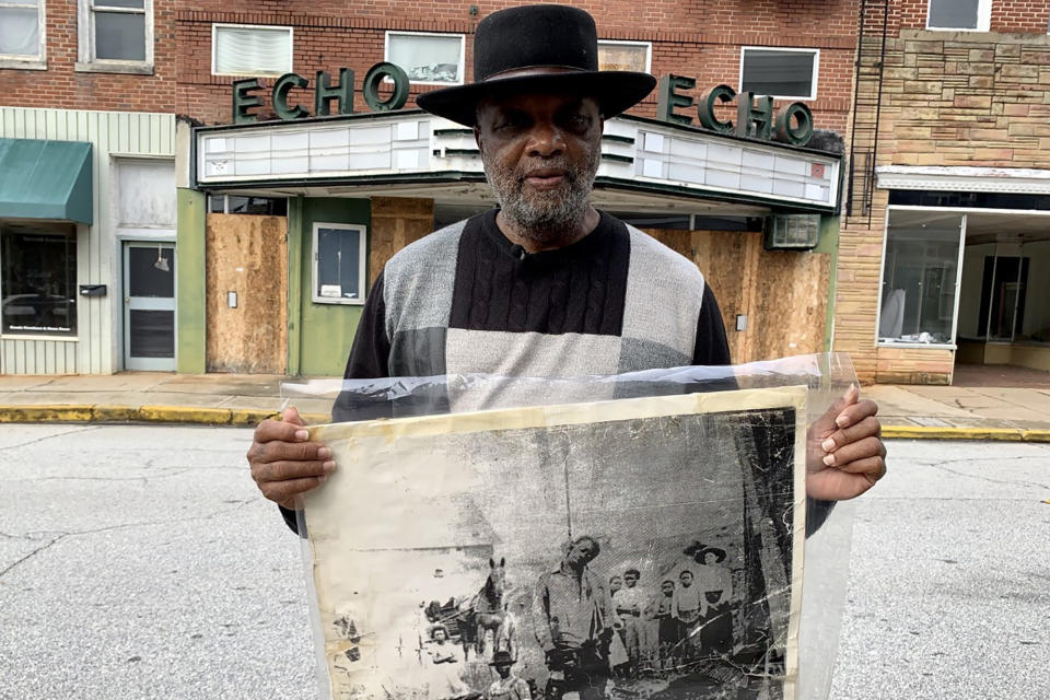 El reverendo David Kennedy fotografiado frente al Teatro Echo, con una foto de su tío abuelo, que murió ahorcado por una turba en Laurens, Carolina del Sur. Kennedy es hoy propietario del teatro, que no hace mucho fue un museo museo y sala de reuniones del Ku Klux Klan. Desea transformar el teatro en un monumento a la reconciliación. Foto del 13 de enero del 2020. (AP Photo/Sarah Blake Morgan)