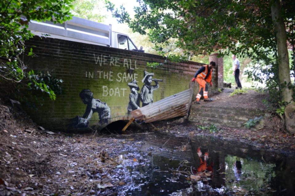 A man in orange overalls removes part of the piece of street art (PA) (PA Media)