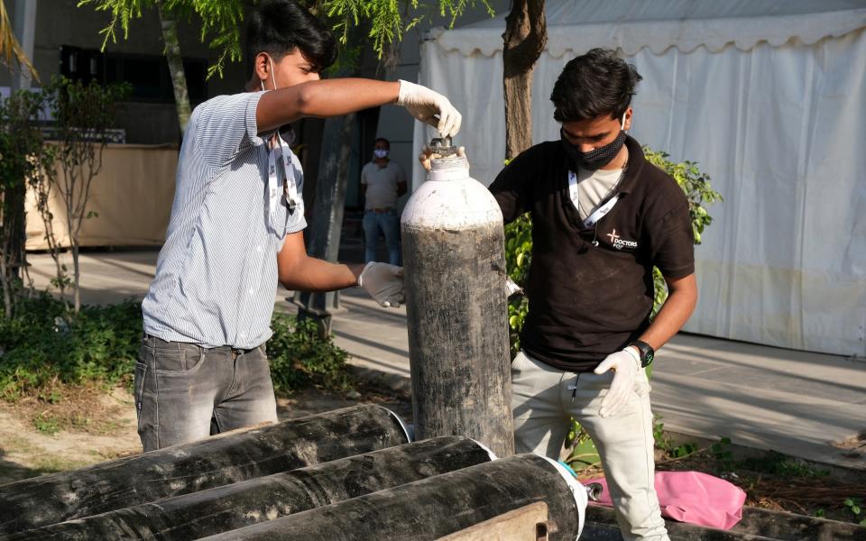 Health workers unload oxygen tanks from a cart at the Covid-19 Care Center set up at the Commonwealth Games Village Sports Complex in New Delhi, India - T. Narayan/Bloomberg