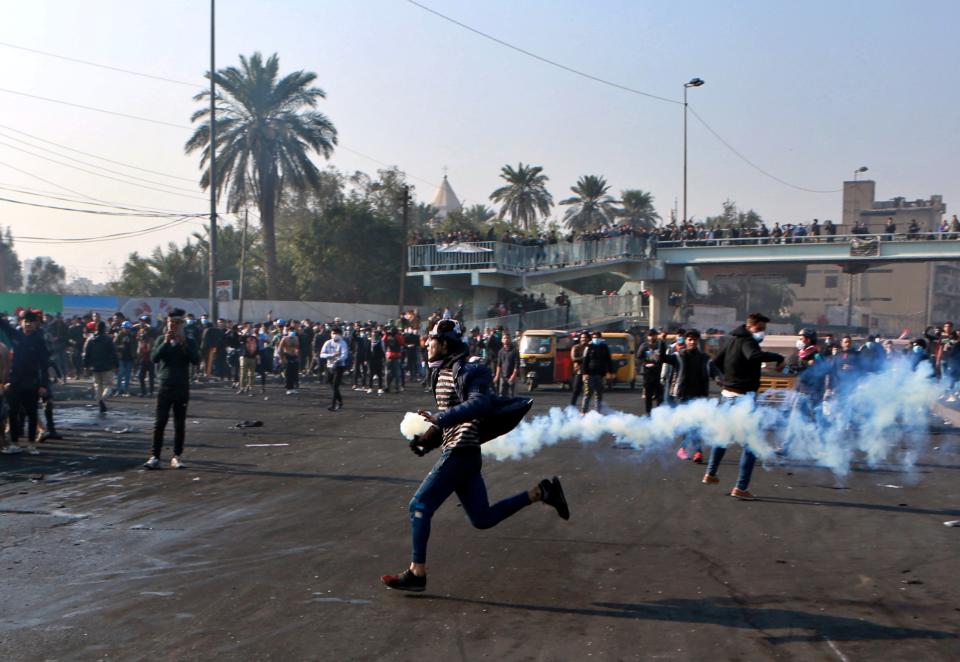 A protester grabs a tear gas canister fired by security forces during clashes in central Baghdad, Iraq, Monday, Jan. 20, 2020. Iraqi security forces also used live rounds, wounding over a dozen protesters, medical and security officials said, in continuing violence as anti-government demonstrators make a push to revive their movement in Baghdad and the southern provinces. (AP Photo/Khalid Mohammed)