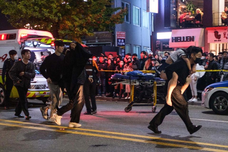 A man carries a woman, who was injured in a Halloween stampede, toward an ambulance (AFP via Getty Images)