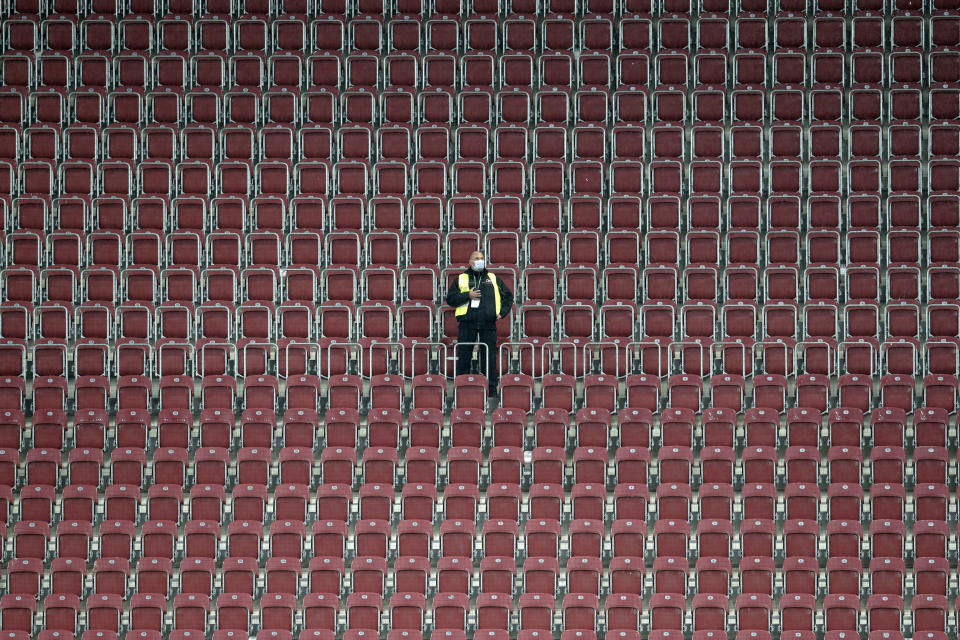 FILE - In this June 17 2020 file photo, a security wearing a face mask to prevent the spread of the new coronavirus stands on the empty tribune of the WWK Arena during the German Bundesliga soccer match FC Augsburg against TSG 1899 Hoffenheim in Augsburg, Germany, Wednesday. More than 50,000 people have died after contracting COVID-19 in Germany, a number that has risen swiftly over recent weeks as the country has struggled to bring down infection figures. (AP Photo/Michael Probst, File)