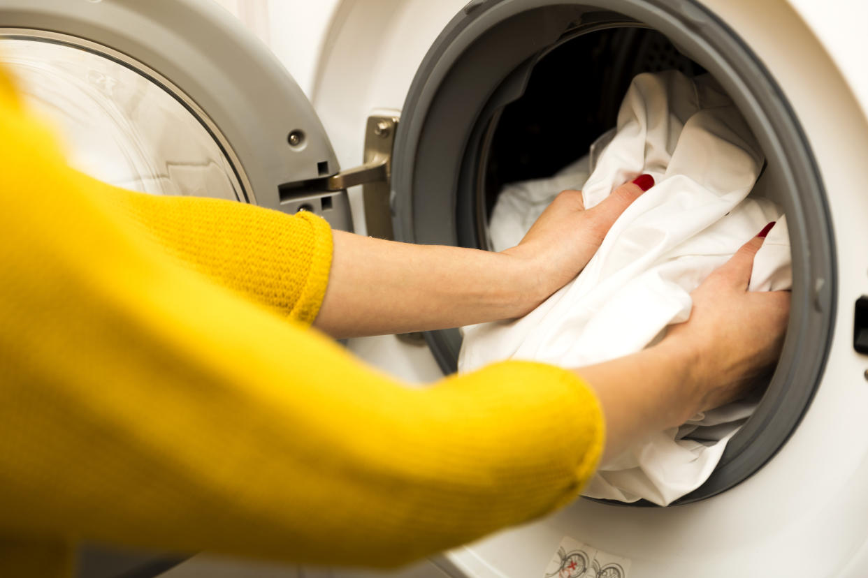 Woman hand loading dirty clothes in washing machine dryer sheets