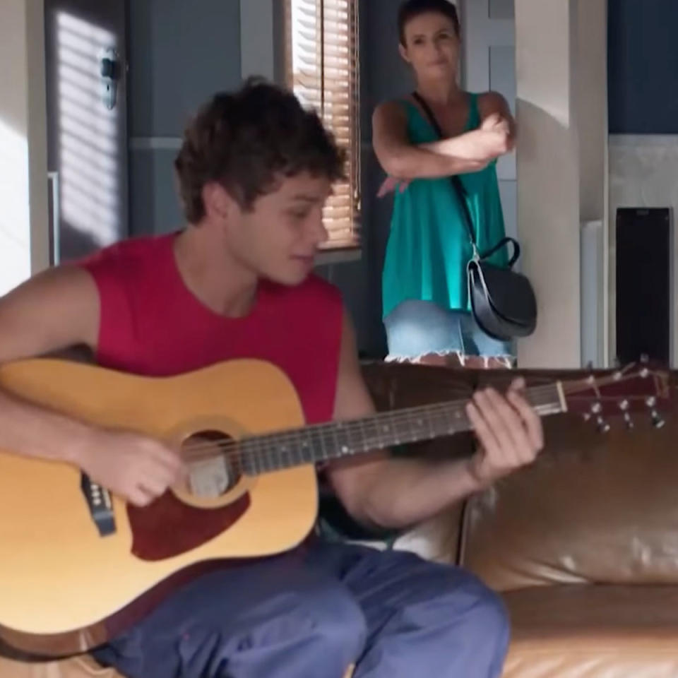 Matt Evans playing the guitar on the set of Home and Away with Ada Nicodemou watching.