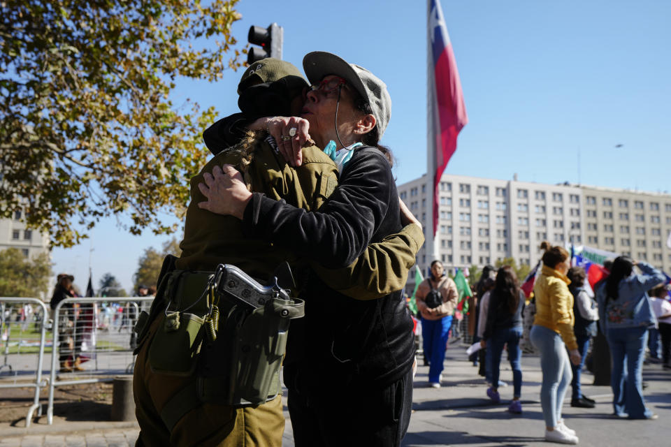 A woman embraces a Chilean police officer during a demonstration seeking justice for police officers killed in the line of duty, in front of the La Moneda presidential palace in Santiago, Chile, Saturday, April 27, 2024. Three police officers were killed early Saturday, in Cañete, Chile's Bío Bío region. (AP Photo/Esteban Felix)
