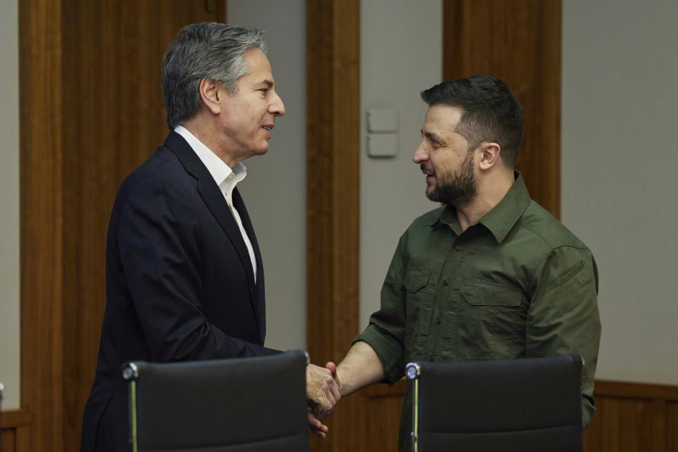 Antony Blinken and Volodymyr Zelensky speak as they shake hands.