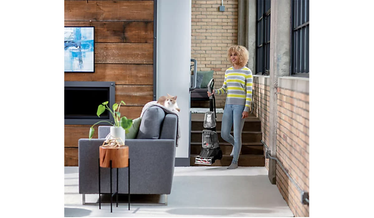 Woman carrying Bissell carpet cleaner through clean carpeted living room