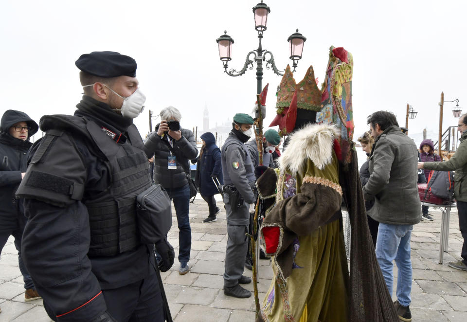 A policeman wearing a sanitary masks passes by a reveler in Venice, Sunday, Feb. 23, 2020. Italian authorities have announced they are shutting down Venice's famed carnival events in a bid to stop the spread of the novel virus, as numbers of infected persons in the country have soared to at least 133, the largest amount of cases outside Asia. (AP Photo/Luigi Costantini)