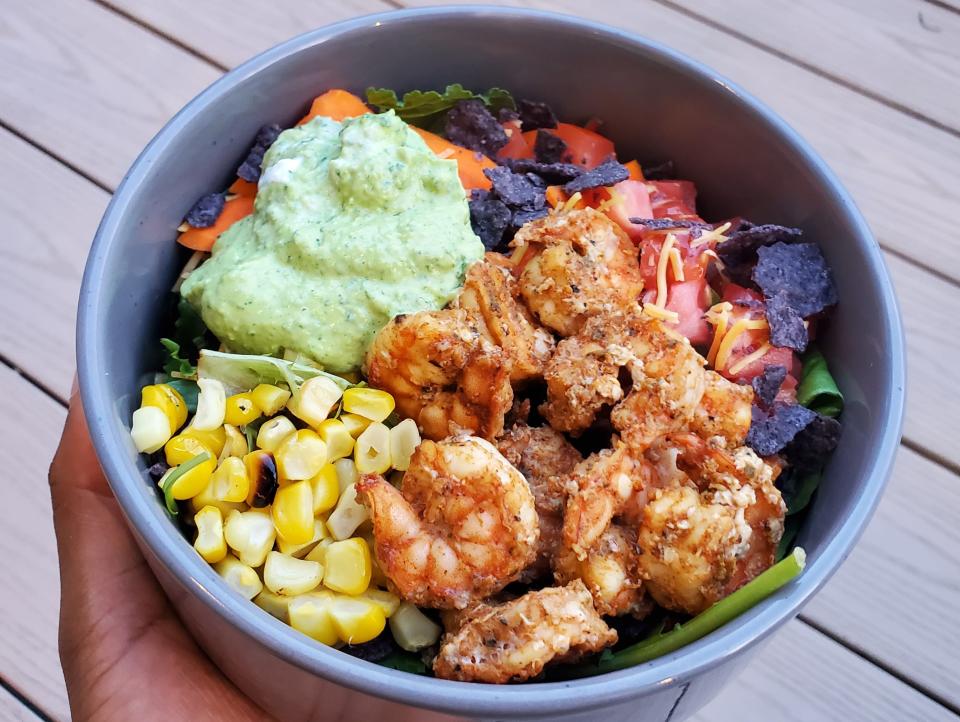 hand holding bowl of salad with greens, corn, shrimp, and green dressing