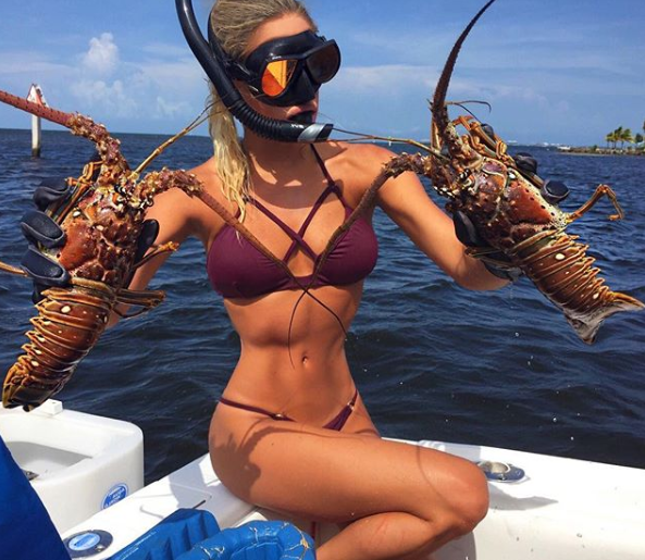 A photo of the 'World's sexiest extreme fisher' Emily Reimer wearing a blue bikini on a boat with two crayfish.