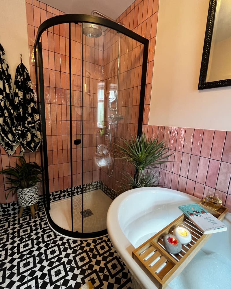 Glass shower door in bathroom with pink subway wall tiles and black and white floor tiles.