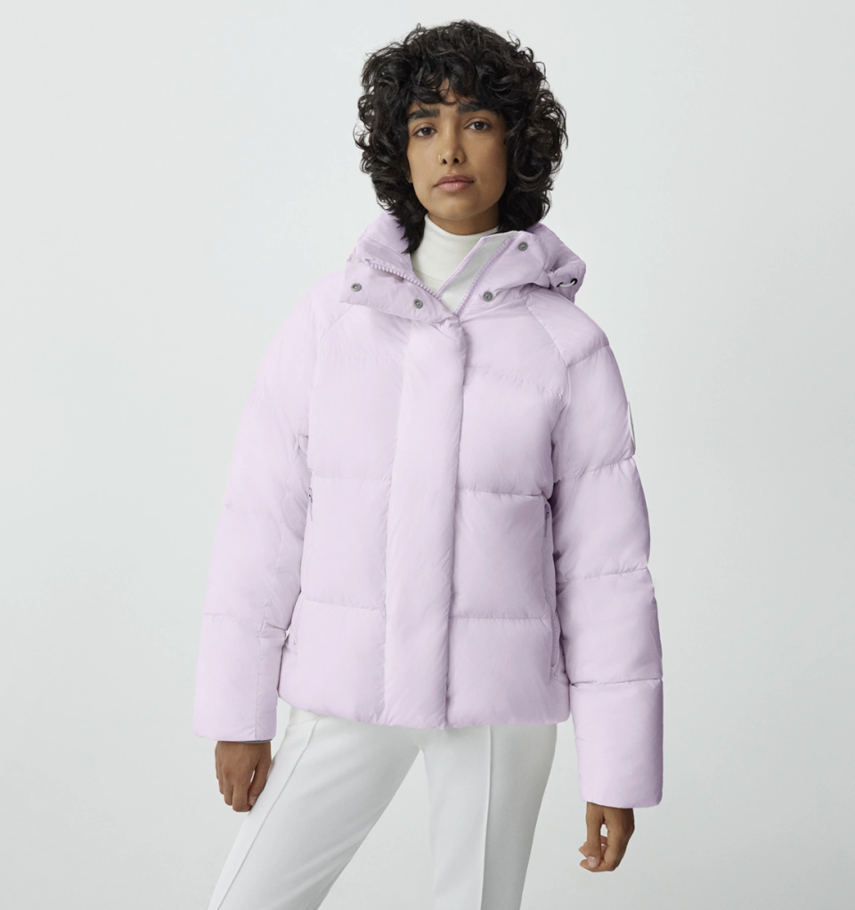 model wearing white pants and pastel light pink Junction Parka Pastels in Sunset Pink (Photo via Canada Goose)