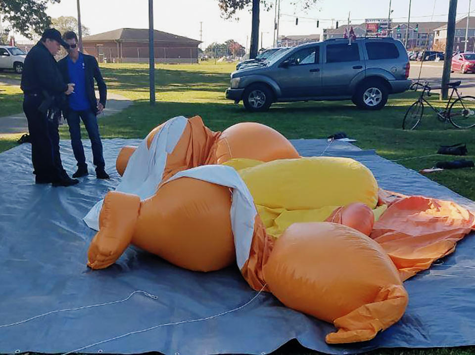 Un policía y un hombre no identificado, de pie junto a un globo con forma de caricatura de Donald Trump, desinflado luego de ser tajeado por una persona en el Parque Monnish cuando varias personas protestaban por la visita del presidente de Estados Unidos a un partido universitario de fútbol americano entre Louisiana State y Alabama, que se disputaba cerca en Tuscaloosa, Alabama, el sábado 9 de noviembre de 2019. (Stephanie Taylor/The Tuscaloosa News via AP)