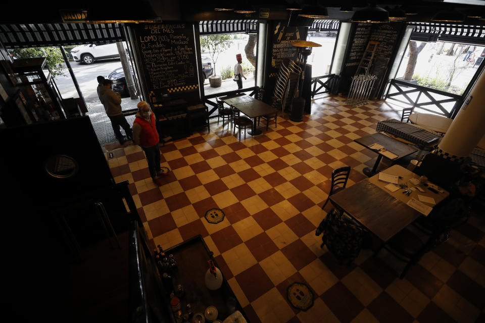 Employees waiting to help takeout customers stand inside the emptied-out ground floor of two-story Argentine steakhouse Quebracho, in the Cuauhtemoc neighborhood of Mexico City, Sunday, Jan. 10, 2021. Worried about its survival, Quebracho is one of many restaurants in the capital and adjacent Mexico State which are banning together in a campaign dubbed "Abrir o Morir," Spanish for "Open or Die," and plan to open their doors to diners again on Monday in defiance of ordinances limiting restaurants to takeout service while the Mexico Valley remains under a COVID-19 pandemic red alert. (AP Photo/Rebecca Blackwell)