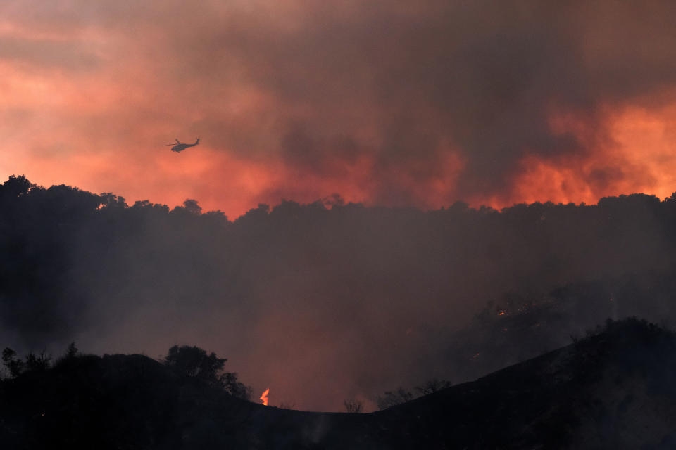 A firefighting helicopter prepares to drop water onto a brush fire scorching at least 100 acres in the Pacific Palisades area of Los Angeles on Saturday, May 15, 2021. (AP Photo/Ringo H.W. Chiu)