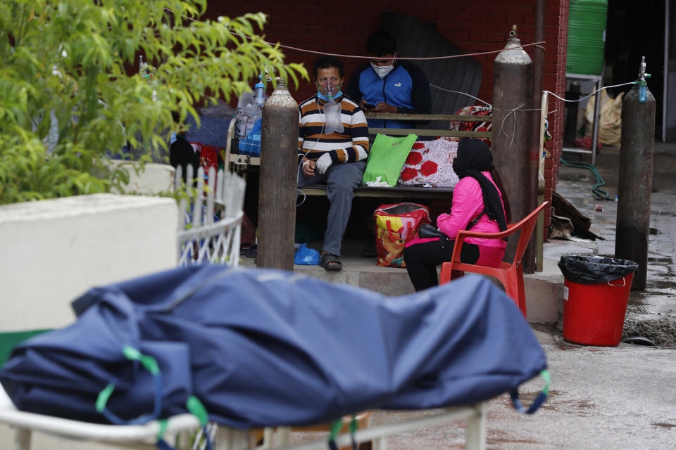 A patient receives oxygen as body of a COVID-19 patient lies covered on a stretcher outside an emergency ward of a government run hospital in Kathmandu, Nepal, Wednesday, May 12, 2021. (AP Photo/Niranjan Shrestha)