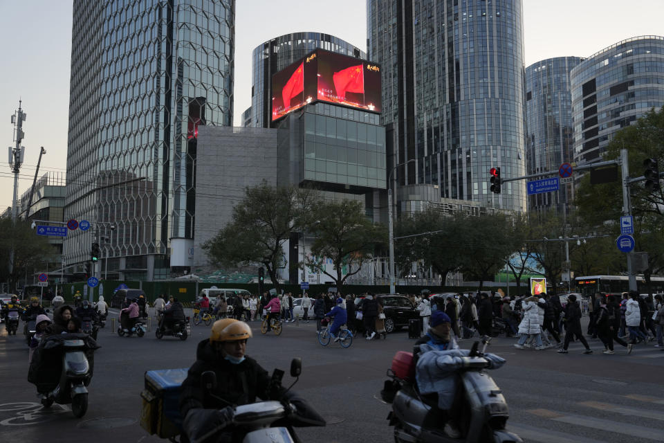 Residents past near an office and retail district with a screen showing the Chinese national flag in Beijing, Saturday, Nov. 18, 2023. Chinese leaders have wrapped up a two-day annual meeting to set economic priorities for the coming year, the official Xinhua News Agency reported Tuesday Dec. 12, 2023 without giving details of what was decided. (AP Photo/Ng Han Guan)