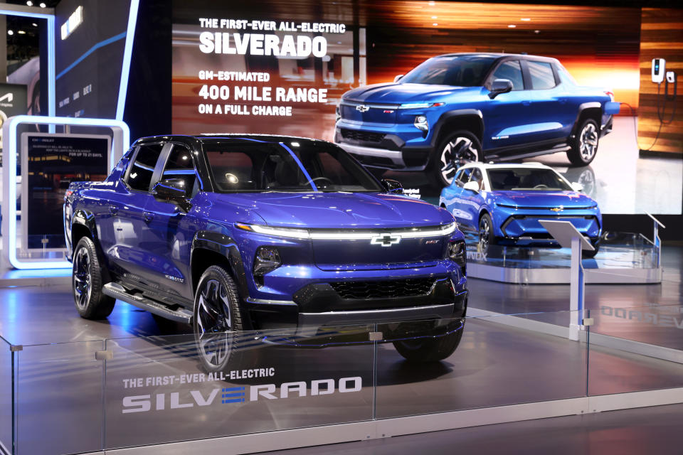 A blue Chevrolet Silverado EV truck is shown on display at an auto show.