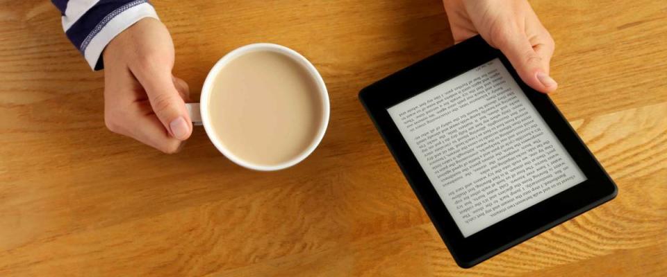 Woman reading a novel on a tablet and drinking her coffee.