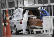 Funeral workers wearing protective gear as a precaution amid the new coronavirus pandemic push the remains of a COVID-19 victim into a funeral car at a field hospital in Leblon, Rio de Janeiro, Brazil, Thursday, June 4, 2020. (AP Photo/Silvia Izquierdo)