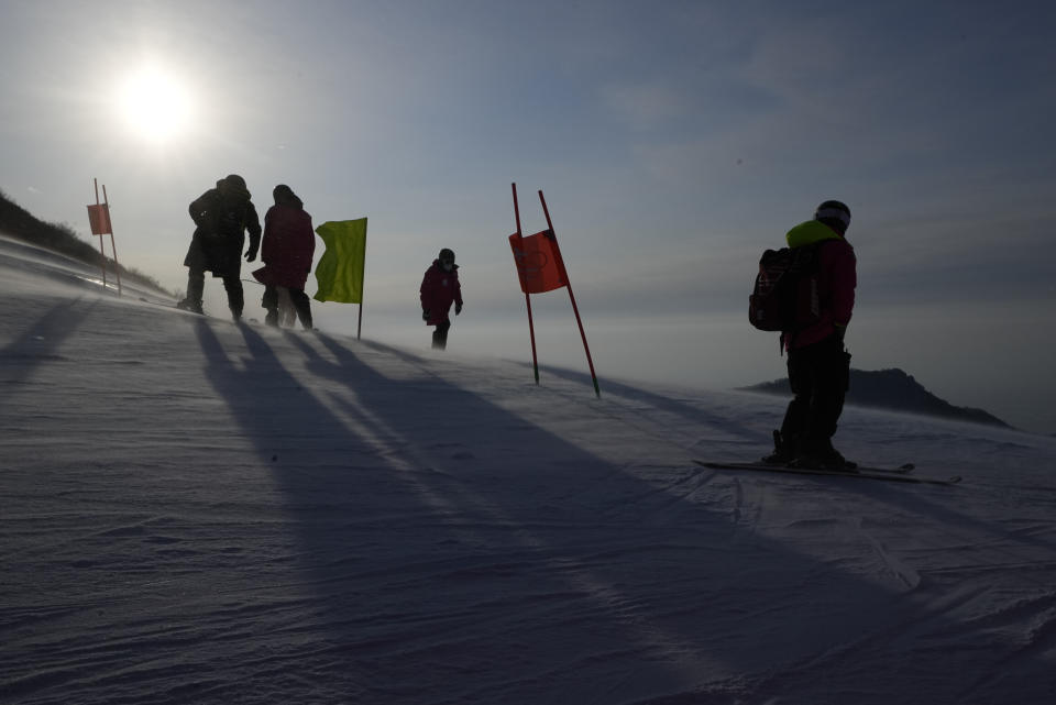 Officials stand on the course as a gust of wind blows powder snow across the slopes of the course for the women's combined downhill at the 2022 Winter Olympics, Thursday, Feb. 17, 2022, in the Yanqing district of Beijing. (AP Photo/Robert F. Bukaty)