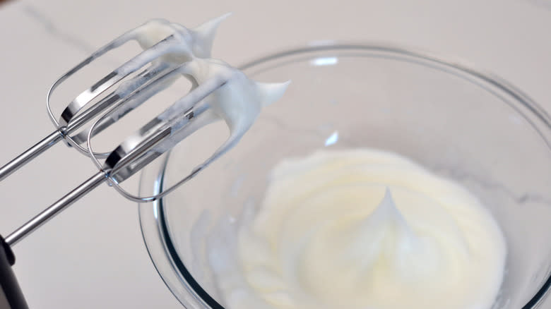 whisked egg whites in glass bowl, peaks on whisk attachments