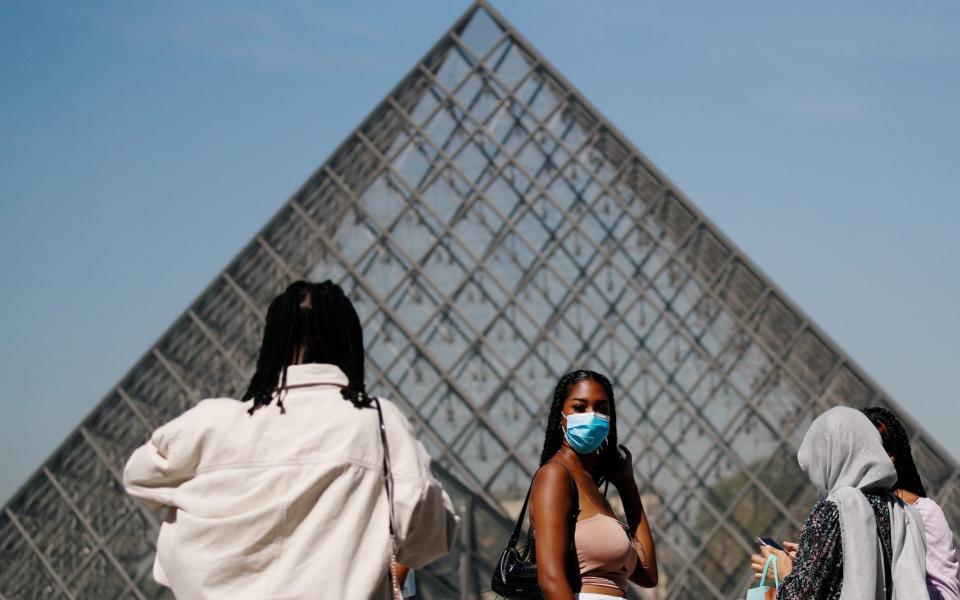 A woman wearing a protective mask walks near the Louvre - GONZALO FUENTES/REUTERS