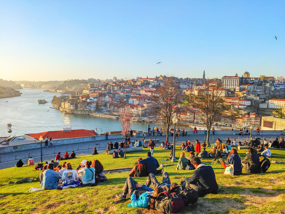 PORTO, PORTUGAL - 21 FEBRUARY, 2022: People sitting on the green lawn, Ribeira view, Porto cityscape in sunlight with Douro river