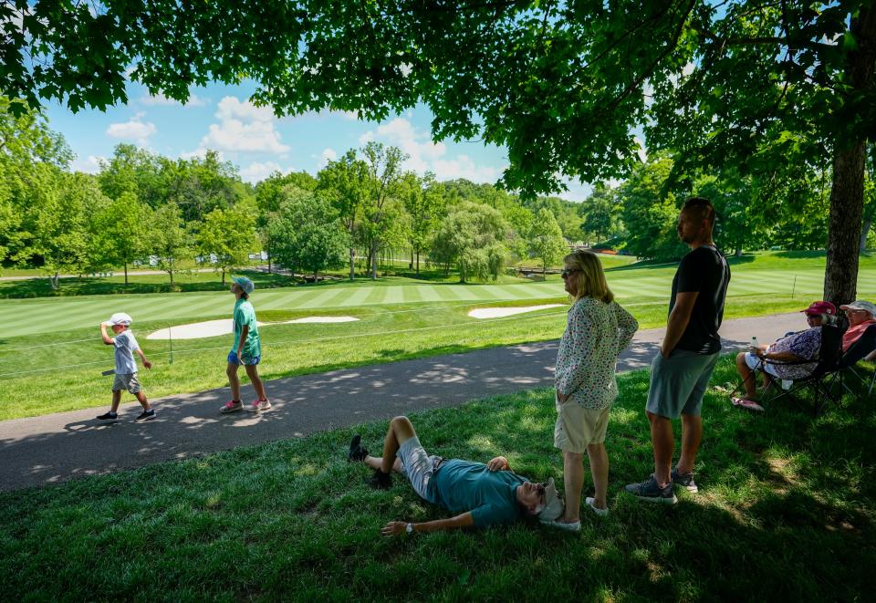 Paul Fiebig, 66, of Galloway, takes a rest on the foot of his wife, Joyce, 69, as they and their son, 39-year-old Mike, wait for golfers Tuesday in the shade beside the 18th fairway during a practice round of the Memorial Tournament at Muirfield Village Golf Club in Dublin.