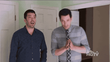 Drew Scott and Jonathan Scott, wearing casual shirts, stand indoors looking surprised and excited, with Drew clapping his hands. The HGTV logo appears