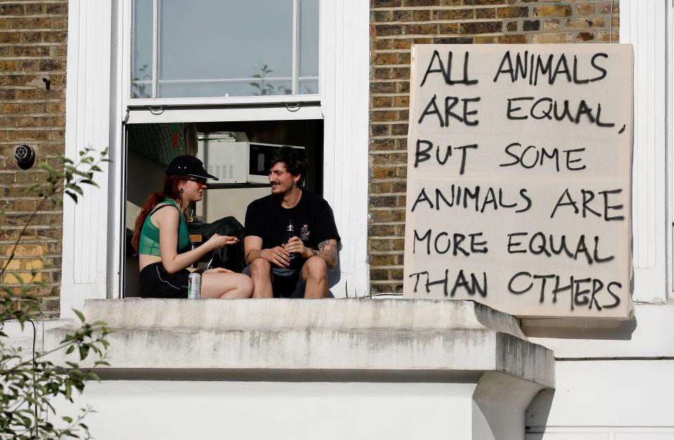 Demonstrators sit on a windowsill with a placards as they protest near the home of 10 Downing Street special advisor Dominic Cummings, in London on May 25, 2020 following his admission he drove and stayed in Durham during the coronavirus lockdown. - British Prime Minister Boris Johnson's top aide Dominic Cummings defied calls to resign on Monday over allegations that he broke coronavirus rules and undermined the government's response to the health crisis. Cummings told reporters that he acted "reasonably and legally" when he drove across the country with his wife while she was suffering from the virus, despite official advice to stay at home. (Photo by Tolga AKMEN / AFP) (Photo by TOLGA AKMEN/AFP via Getty Images)