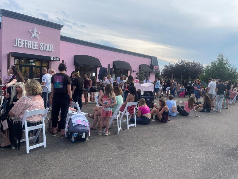 crowds of people in line, some sitting in white folding chairs or on the concrete, in front of the jeffree star store