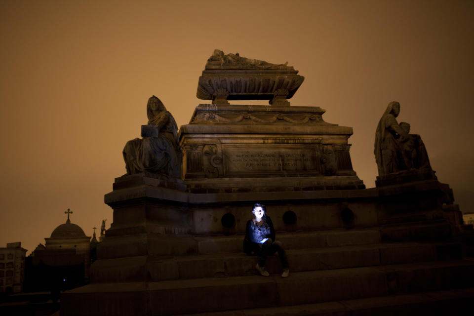 In this Dec. 6, 2012 photo, a girl poses for a picture in front of a tomb as she takes a nighttime guided tour through the Presbitero Matias Maestro cemetery in Lima, Peru. When Presbitero Matias Maestro cemetery in Lima received its first body in 1808, the best plots went to the elite, unless the noble had been dishonored or disgraced. (AP Photo/Rodrigo Abd)