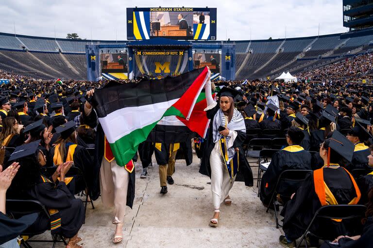 En una ceremonia de graduación en la Universidad de Michigan en un estadio, egresadas Hamamy exhiben una bandera de Palestina; las protestas contra Israel se expanden.