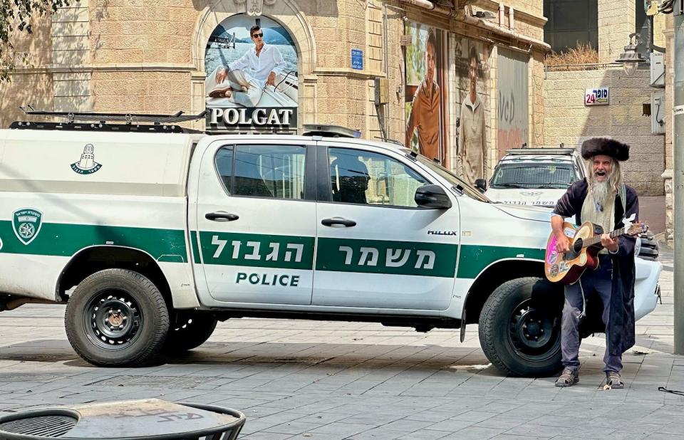 A man carries a guitar past a police truck in Jerusalem.