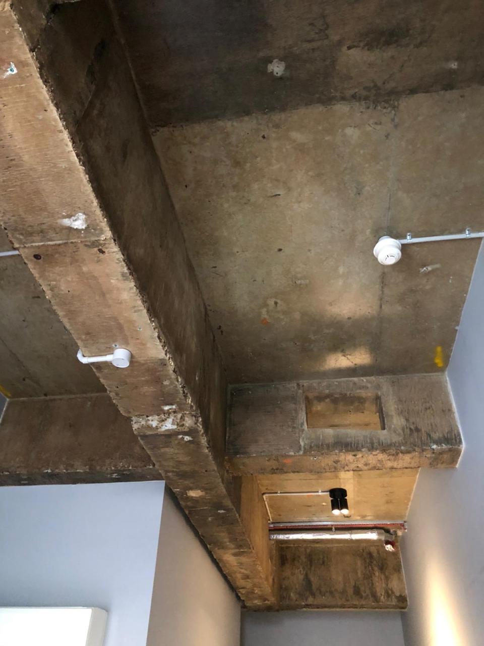 Image shows exposed pipes and naked light bulb on isolation hotel room ceiling