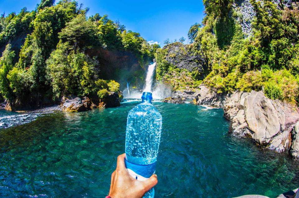 Optical Illusion of a person capturing a waterfall in a bottle.