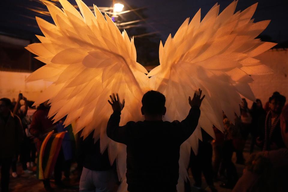 A reveler is silhouetted against a pair of angel wings as they help a trans performer with a costume during a Gay Pride parade marking the culmination of LGBTQ+ Pride month, in Asuncion, Paraguay, Saturday, June 29, 2024. (AP Photo/Jorge Saenz)